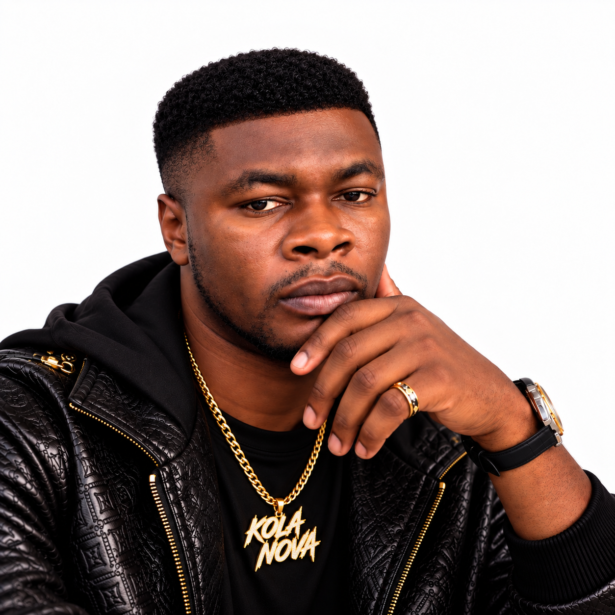 Press portrait of Kola Nova resting his chin on his hand, wearing a textured black jacket and a gold Kola Nova pendant